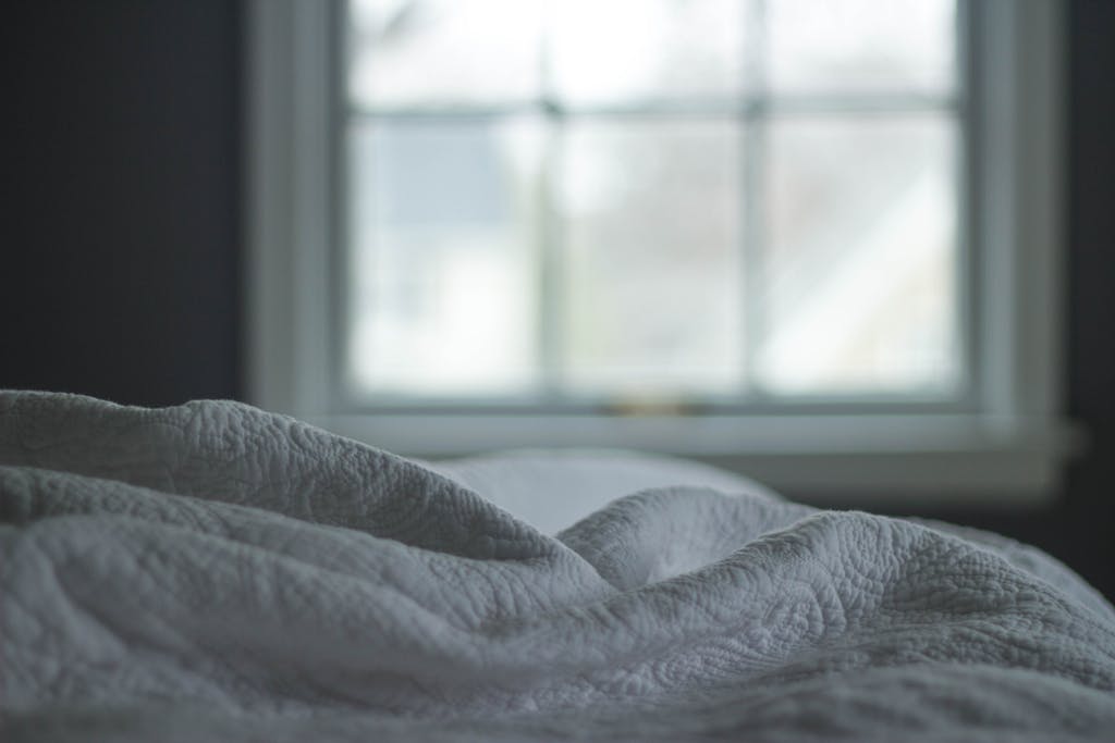 A tranquil bedroom view with a quilted blanket by the window softly lit by morning light, ideal for relaxation themes.
