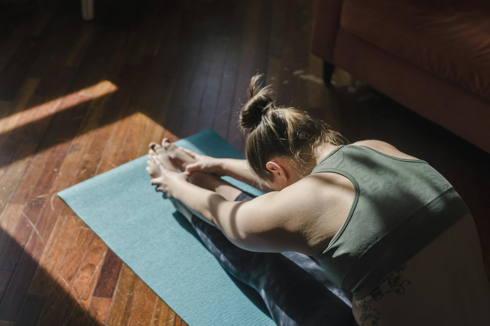 A woman stretches in a yoga pose on a mat in a sunlit room, emphasizing relaxation.